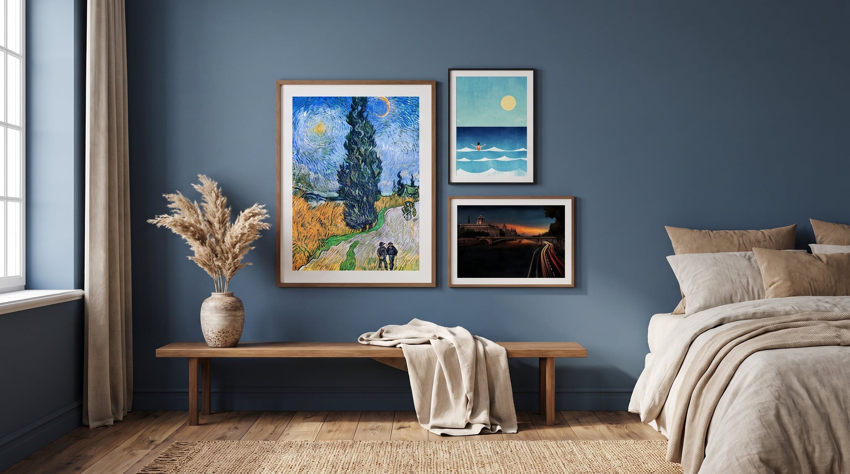 Bedroom with blue framed art in varied sizes above a low wooden bench with dried grasses.